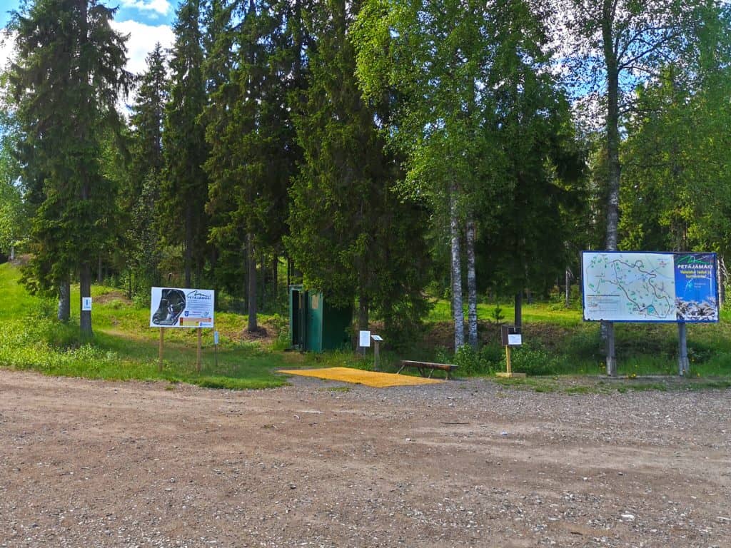 Kesäinen kuva Petäjämäen ulkoilukeskuksesta ja frisbeegolfin heittopaikasta. Kuvassa myös kaksi opastuskylttiä ja puita.